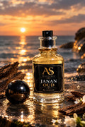 A bottle of AS Fragrance 'Javan Oud' perfume is displayed on a wet rocky shore at sunset, with a black spherical object and small white flowers in the foreground.